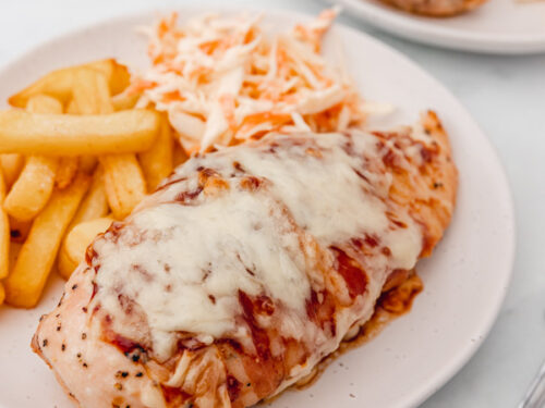 a plate of hunters chicken served with chips and coleslaw.
