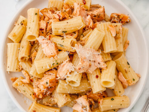 a plate of salmon pasta placed on a white marble surface.