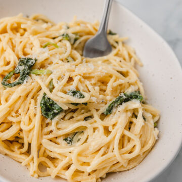 a bowl of creamy pasta with spinach and a fork.
