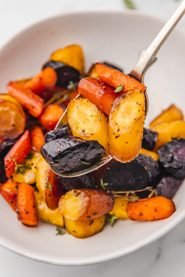roasted rainbow carrots lifted on a serving spoon.
