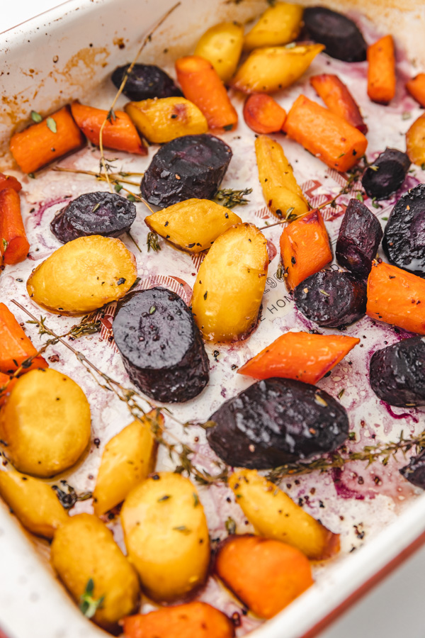 roasted rainbow carrots in a baking tray with thyme leaves.
