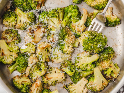 a fork piercing a cooked broccoli floret in a pan.