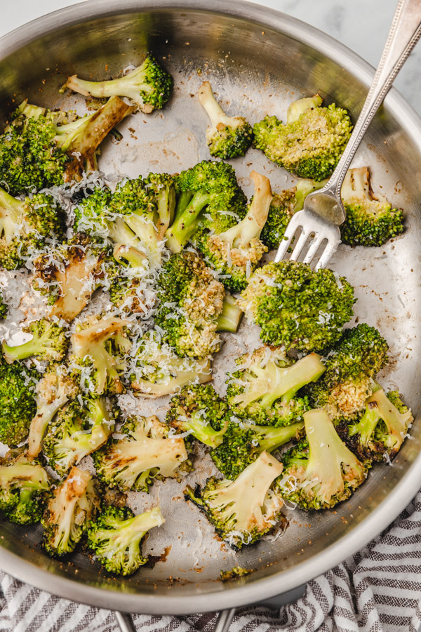a fork pushing broccoli in a skillet.
