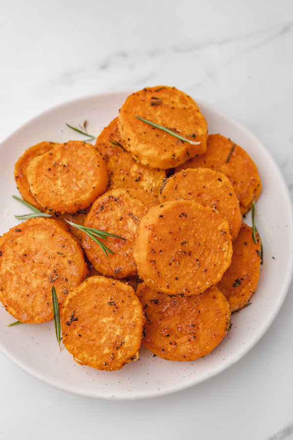 a plate of sweet potato slices garnised wuth fresh rosemary.