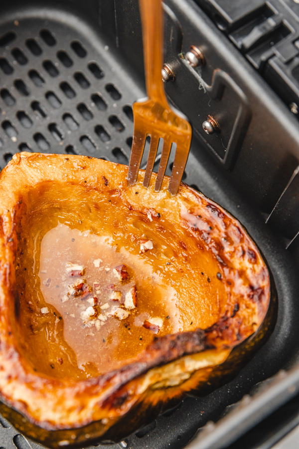 a fork inserted into the fresh of acorn squash placed in an air fryer basket.