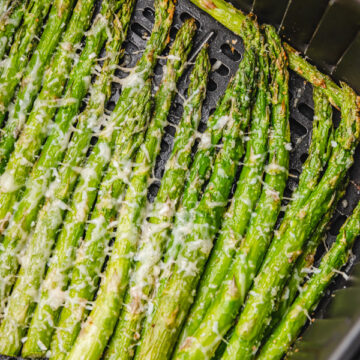 cooked asparagus in air fryer basket garnised with parmesan cheese.
