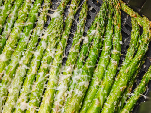 cooked asparagus in air fryer basket garnised with parmesan cheese.