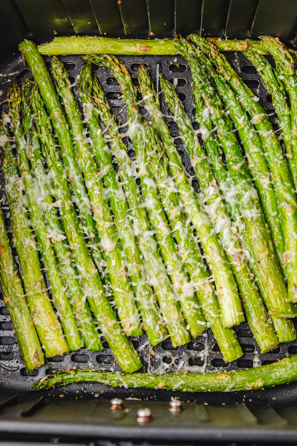 cooked asparagus with parmesan cheese in air fryer basket.