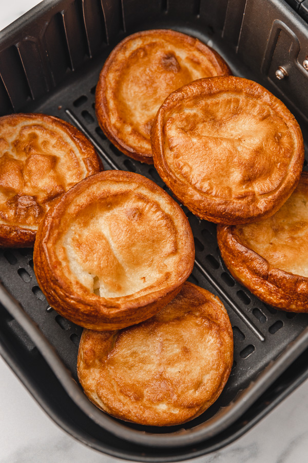 six giant golden brown yorkshire pudding in air fryer basket.