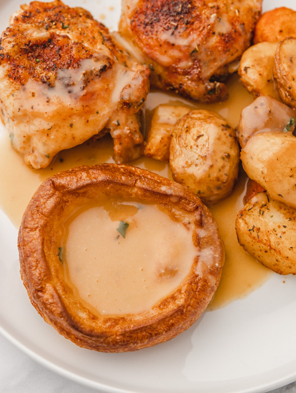 a plate of roast dinner with chicken thighs, carrots, yorkshire pudding and gravy.