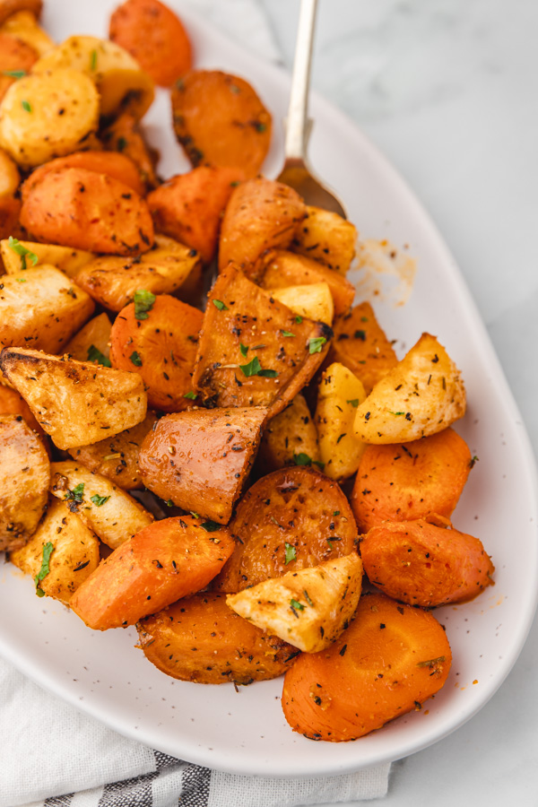 a spoon into a platter of roasted carrots, parsnip and sweet potatoes.