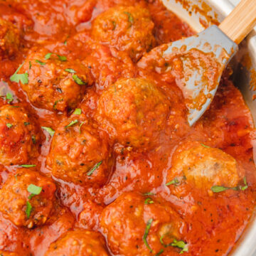a ladle pushing meatball in a pan of meatballs and tomatoes.