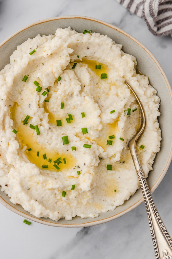 a bowl of creamy boursin cauliflower mash in a bowl with a serving spoon.