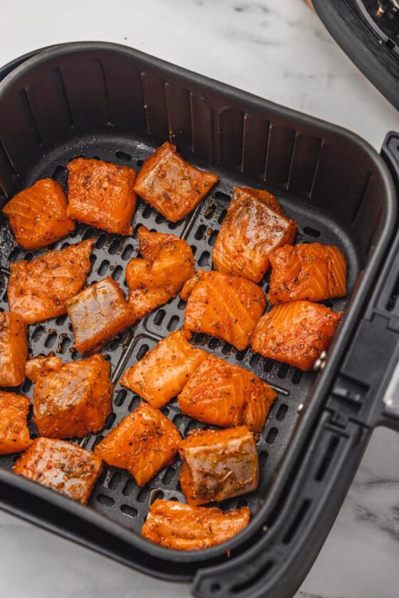uncooked seasoned salmon pieces in a in air fryer basket.