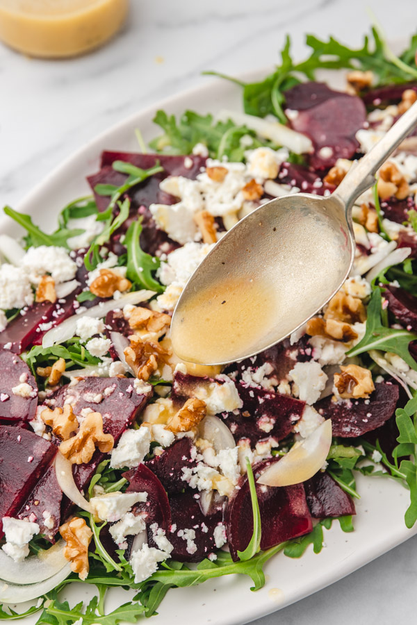 a spoon of honey mustard dressing drizzling on beets salad.