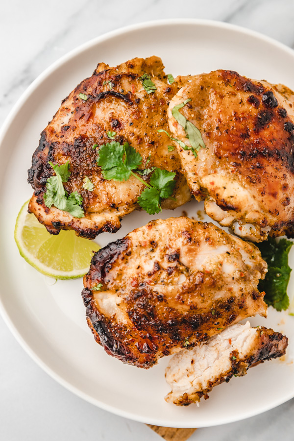 chicken thighs on a plate with lime slices and cilantro leaves as garnish.