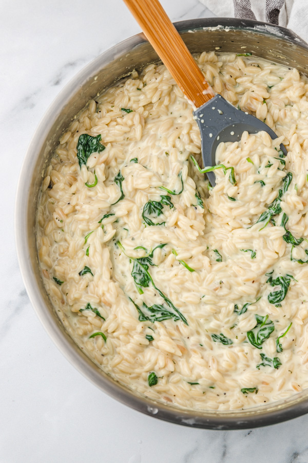 a skillet of cremy orzo with spinach.