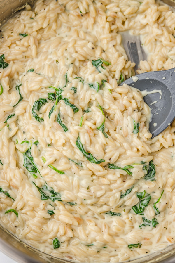 a silicon spatula pushing creamy orzo in a skillet.