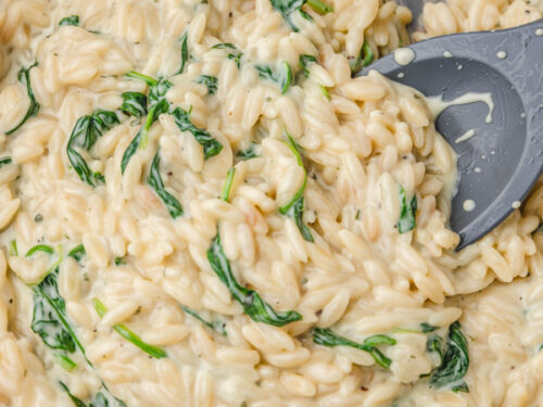 creamy orzo with spinach in a skillet with a silicon spatula stirring it.