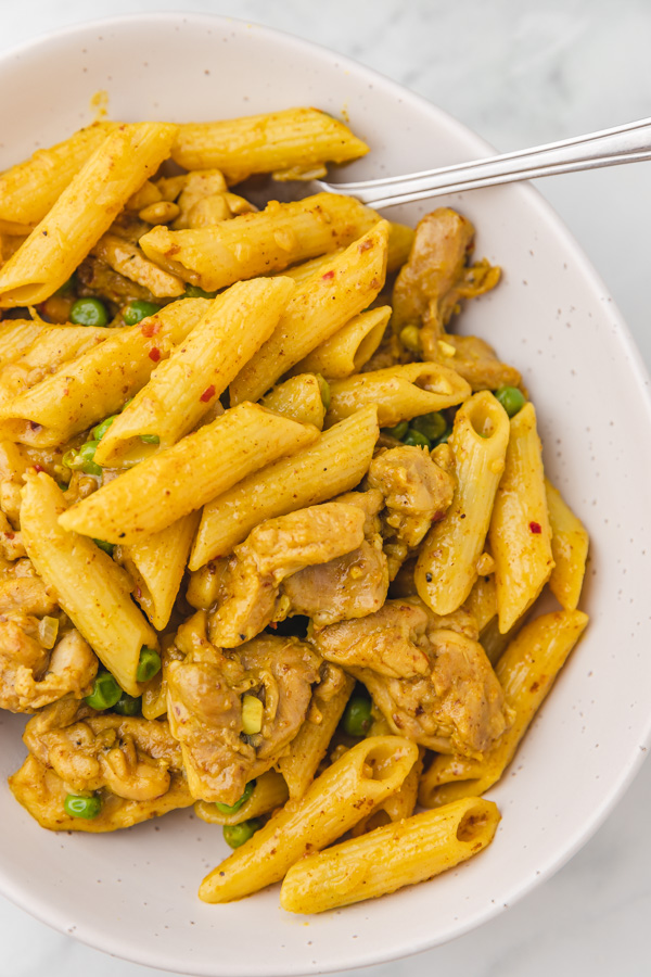 a bowl of curry pasta with chicken and peas.
