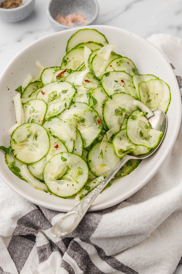 a bowl of cucumber salad placed beside a white and black strip napkin.