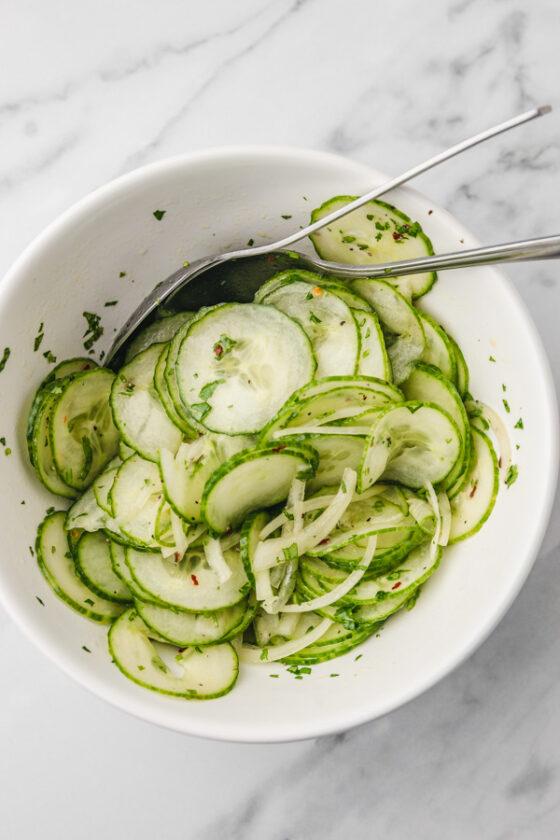 cucumber salad in a white mixing bowl with two spoons.