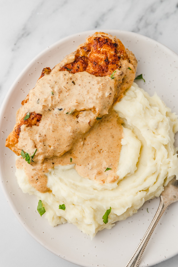 a plate of creamy chicken cutlet sitting on a bed of mashed potatoes.