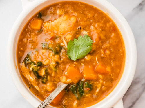 lentil chicken soup in a small white bowl witha spoon.