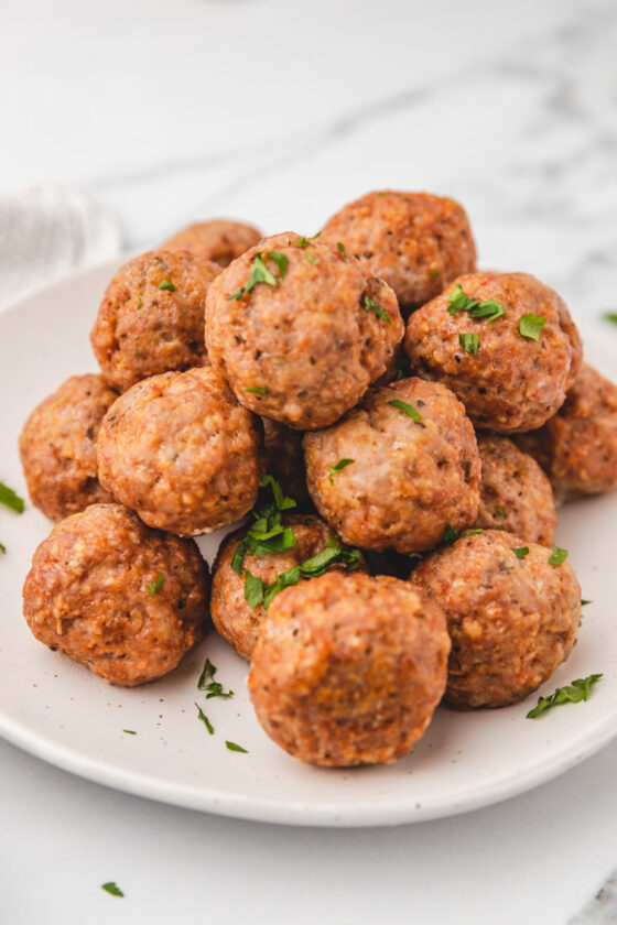 meatballs on a white plate garnished with chopped parsley.
