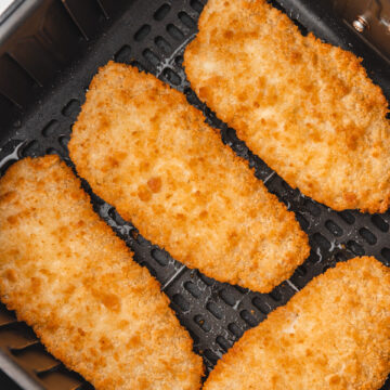 four breaded fish fillets in an air fryer basket.
