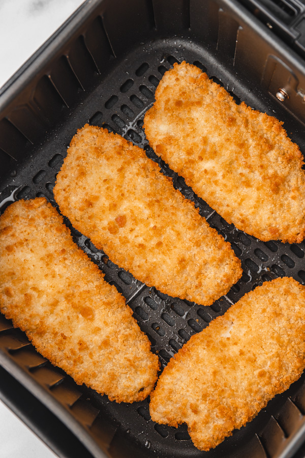 four breaded fish fillets in an air fryer basket.