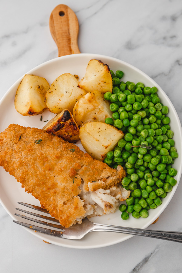 a plate of breaded fish fillet with potatoes and peas.