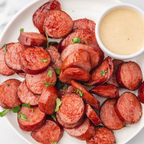 a plate of sliced kielbasa with a small of dipping sauce.