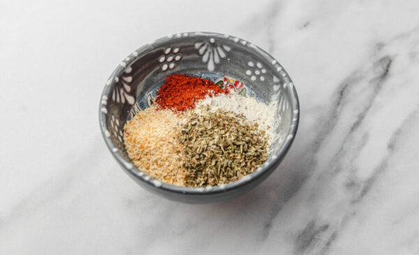 four different herbs and spices measured into a small bowl.