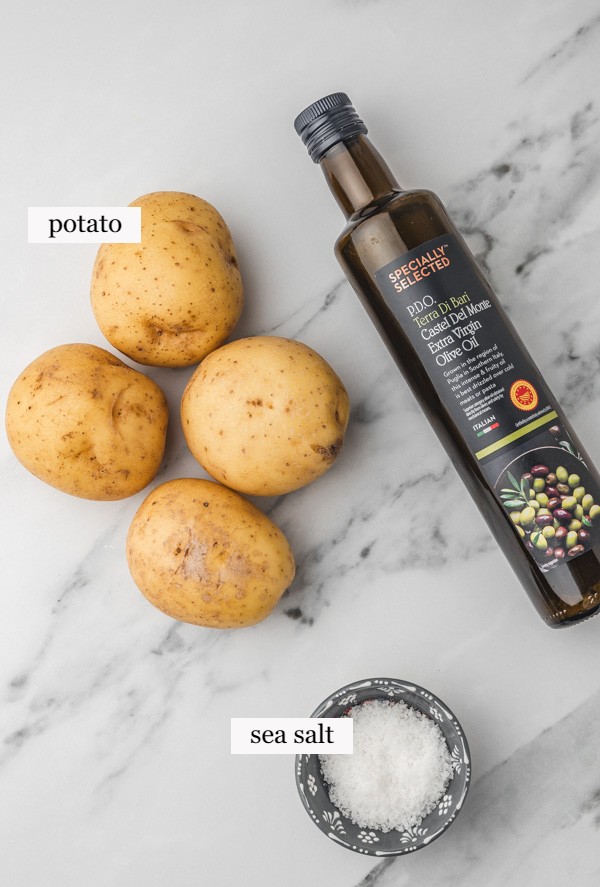 raw potatoes,  a bottle of olive oil and a pot of salt placed on a marble surface.