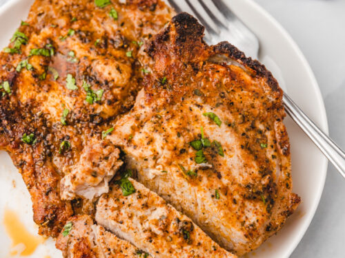 juicy pork chops on a plate with a fork on the the side.