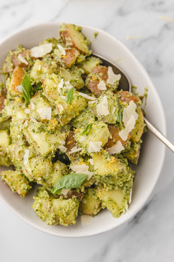 a bowl of pesto potato salad garnished with basil leaves, lemon zest and parmesan cheese.