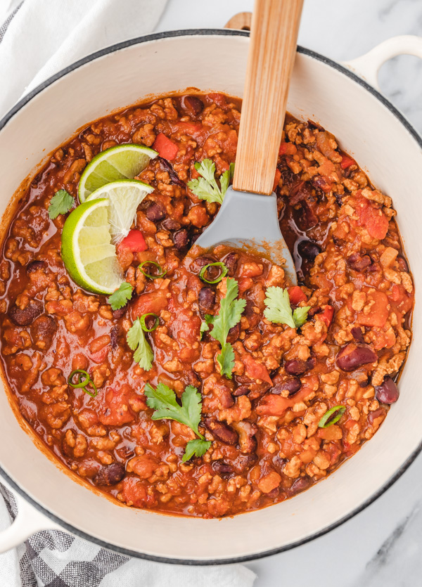 a pot of chili garnished with chopped cilantro and lime slices.