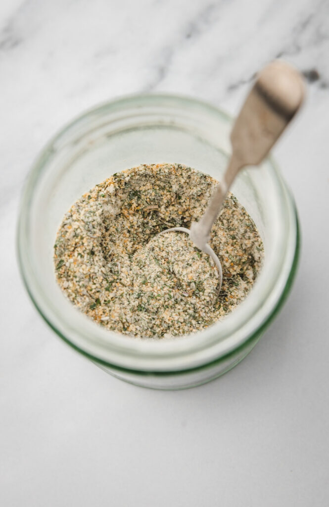 homemade garlic and herb seasoning in a glass jar with a spoon.