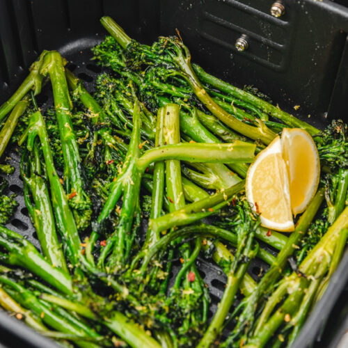 broccolini in air fryer basket garnished with two lemon wedges.
