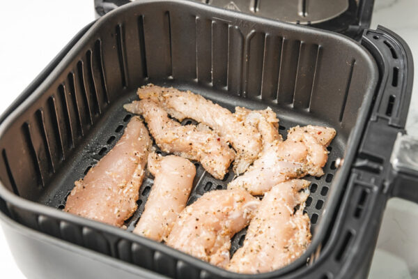 raw seasoned chicken tenders in an air fryer basket,