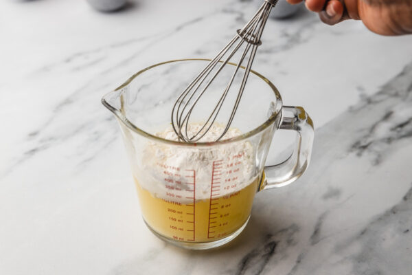 a hand mixing flour and chicken stock in a jug.