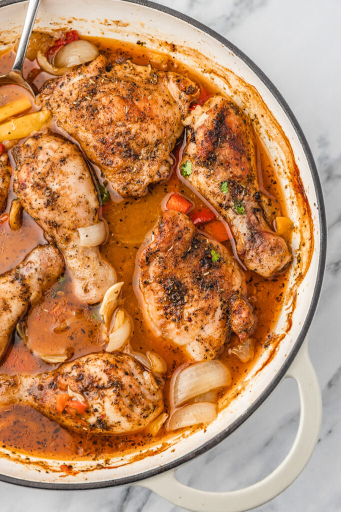 baked chicken thighs and pepper sitting in gravy in a skillet.