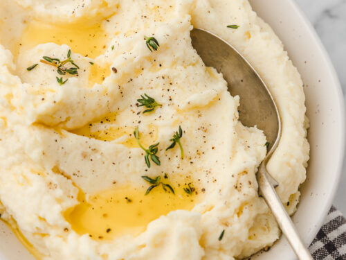 a bowl of ricotta mashed potato drizzled with melted butter and garnished with thyme.