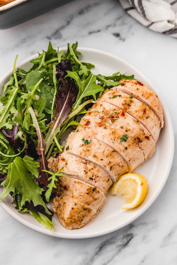 sliced chicken breast and arugula salad on a plate with a lemon wedge.