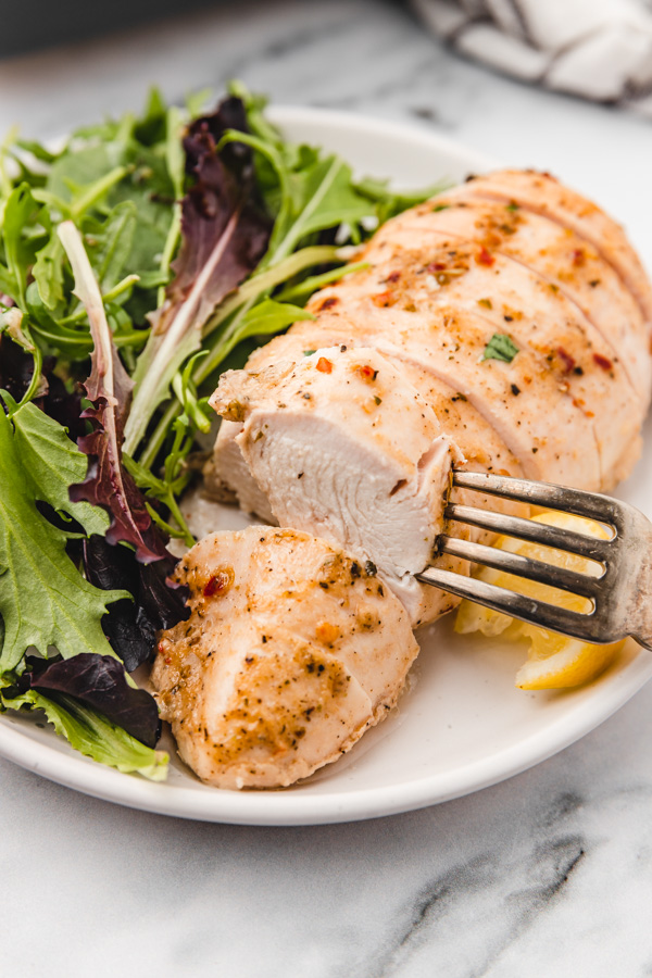 a fork inserted in a sliced chicken breast to show how juicy it is.