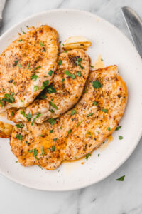three pieces of buttered turkey steaks on a plate.
