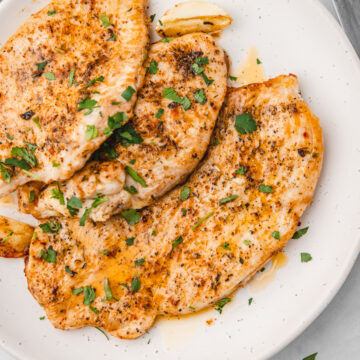 three pieces of buttered turkey steaks on a plate.