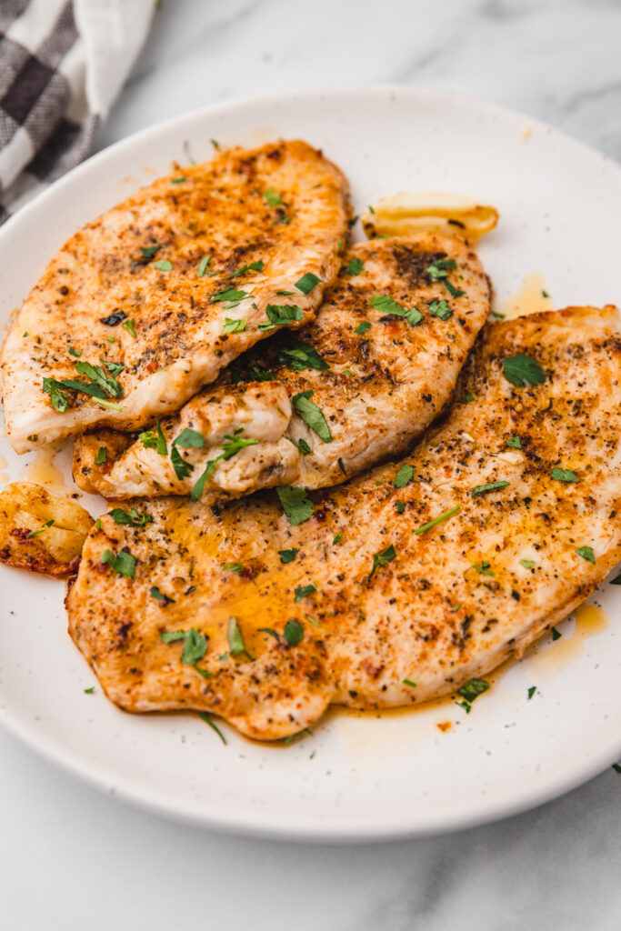 three turkey steaks on a plate with smashed garlic.