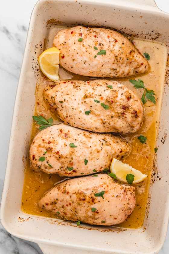 four baked chicken breast in baking dish.